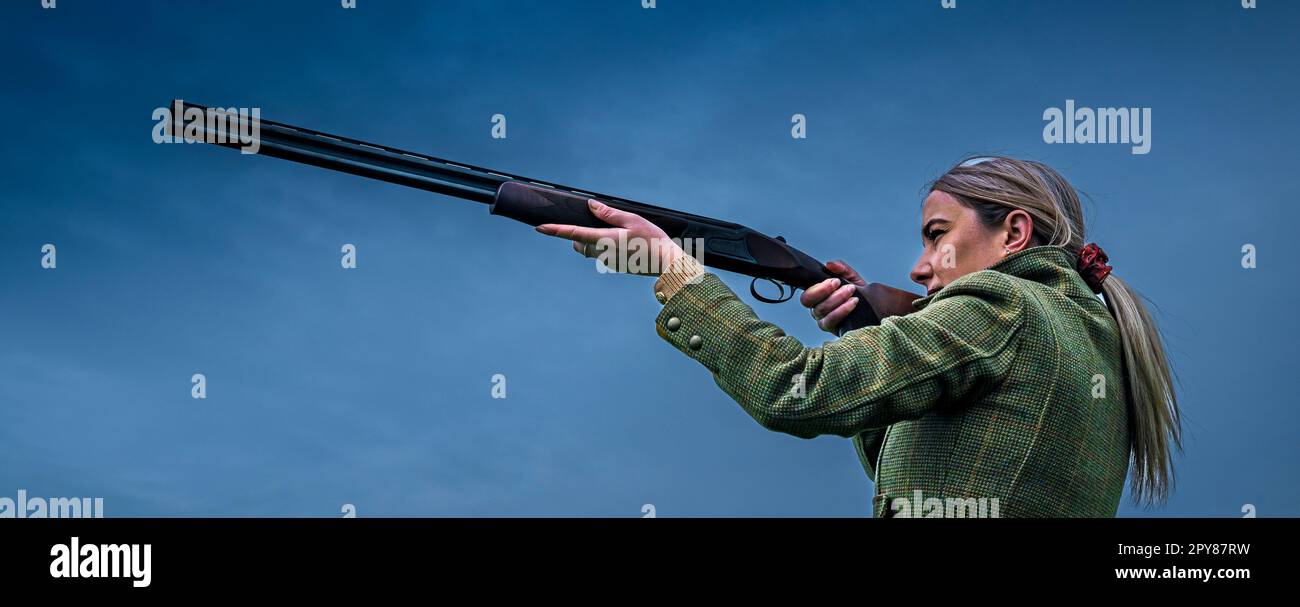 Un portrait d'une femme avec un fusil de chasse contre un ciel bleu Banque D'Images
