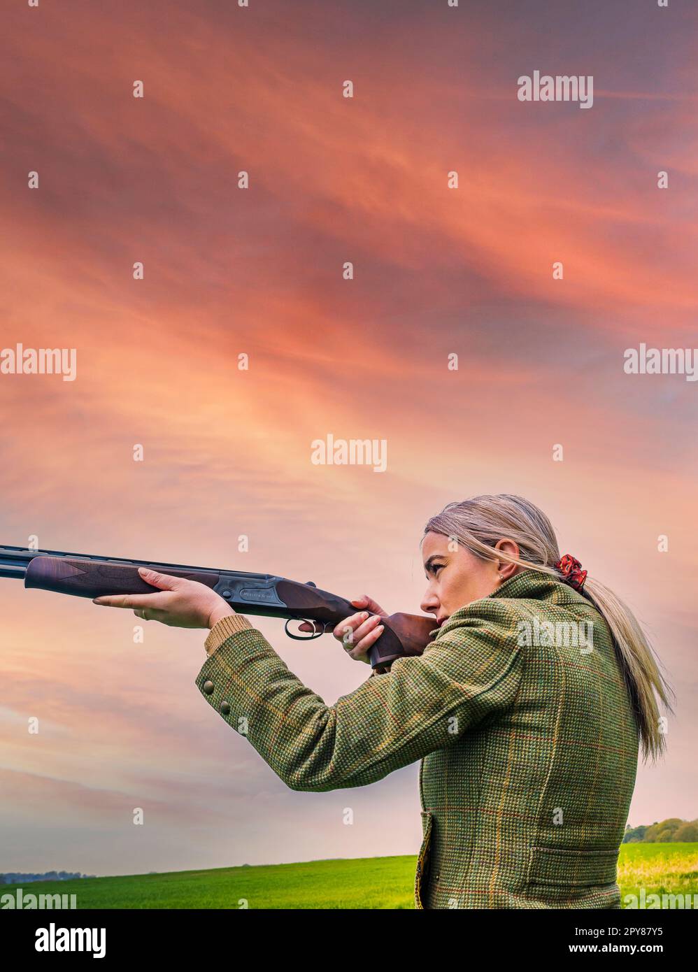 Un portrait d'une femme avec un fusil de chasse contre un ciel du soir au coucher du soleil Banque D'Images