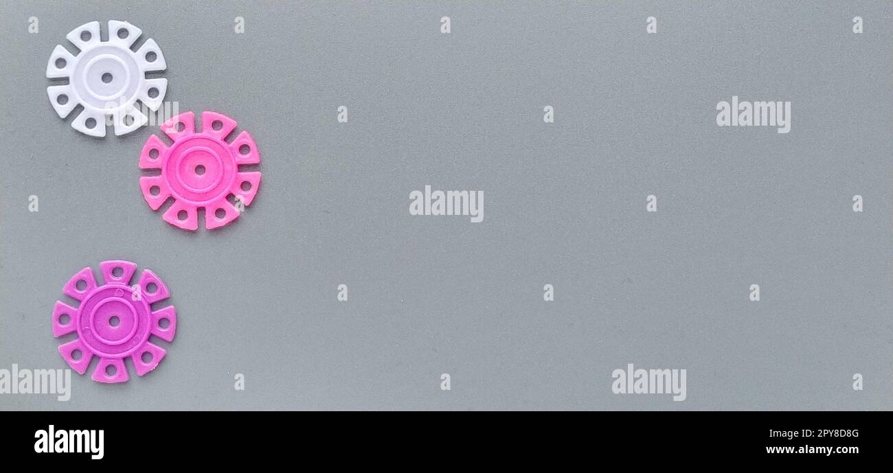 Détails multicolores sous la forme de flocons de neige du designer pour enfants sur fond gris dans la partie gauche de l'image. Disques en plastique blanc et rose pour le développement de la motricité fine Banque D'Images
