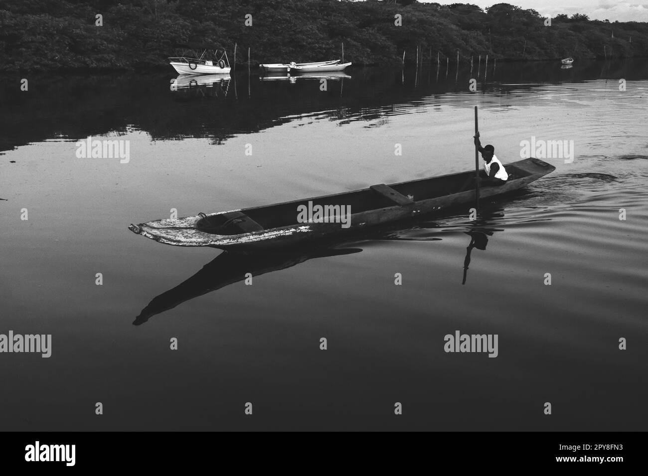 Photographie en noir et blanc d'un pêcheur pagayant son canot sur la rivière Jaguaripe, ville d'Aratuipe, en fin d'après-midi. Banque D'Images