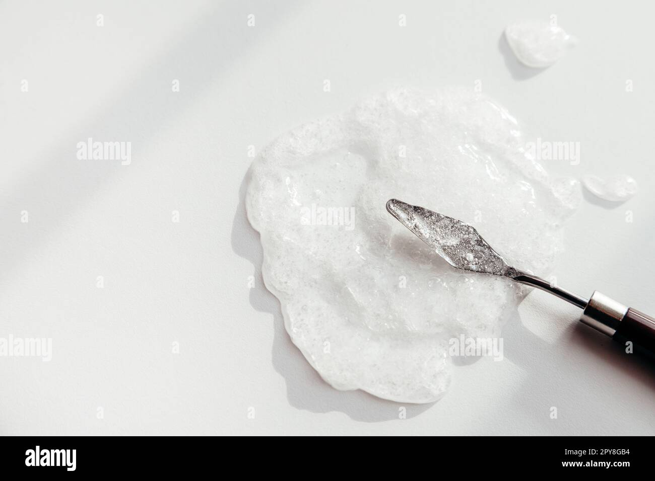 Gel à base de sérum cosmétique avec bulles, mélange par spatule métallique, fond liquide transparent Banque D'Images