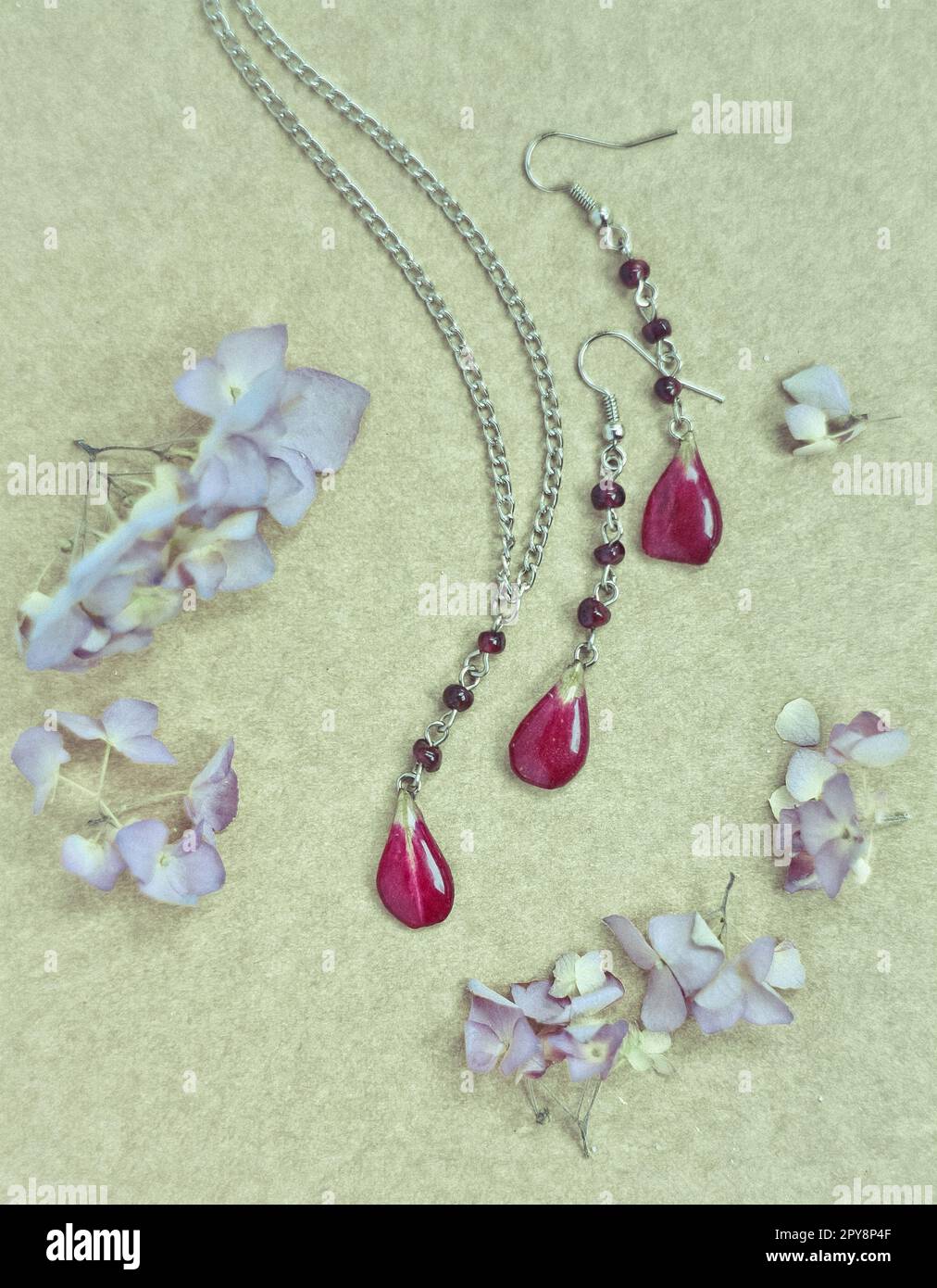 Ensemble de bijoux artisanaux à gros plan avec pétales rouges et fleurs fraîches concept photo Banque D'Images