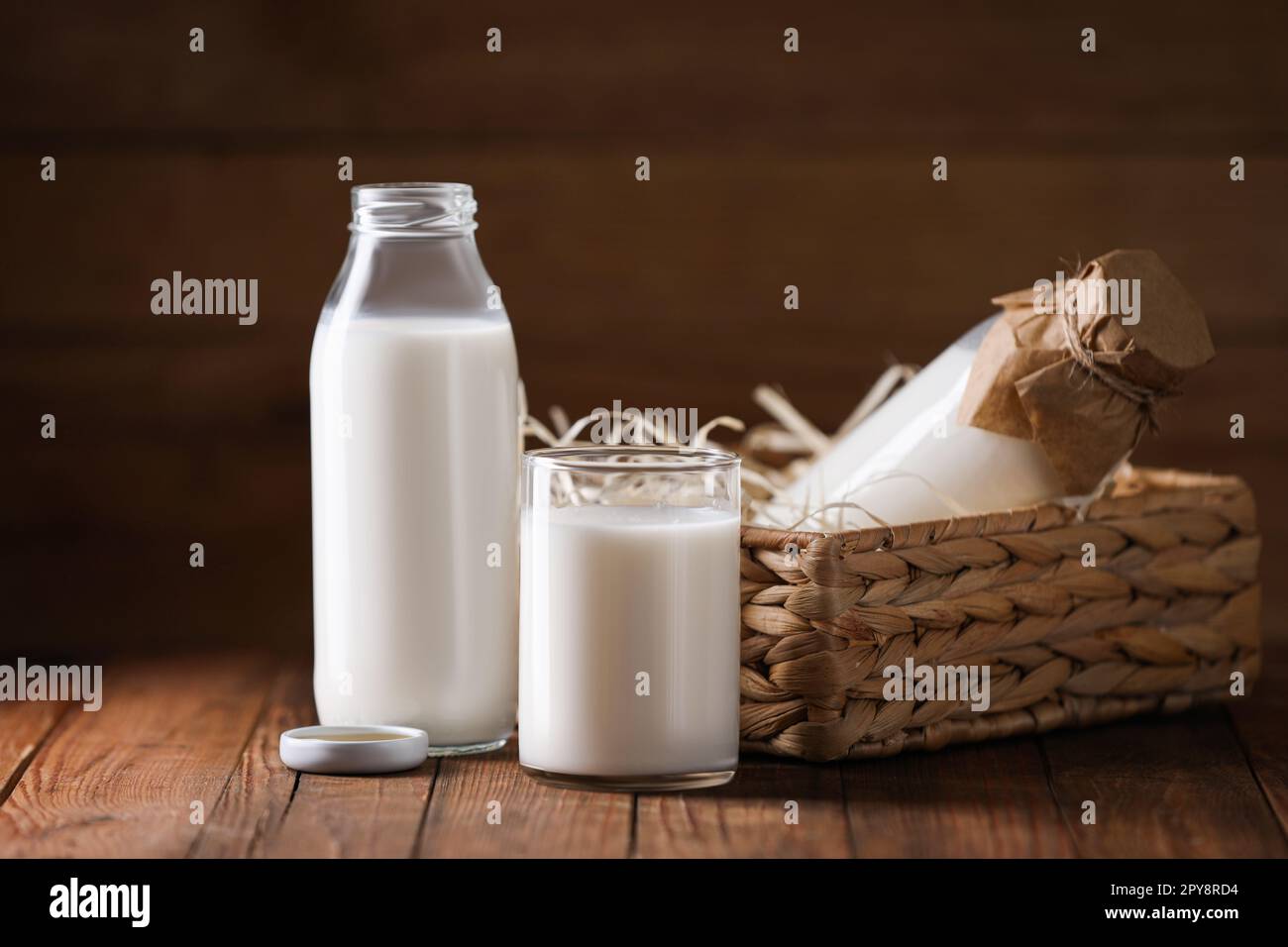 Lait frais savoureux en bouteilles et verre sur table en bois Banque D'Images