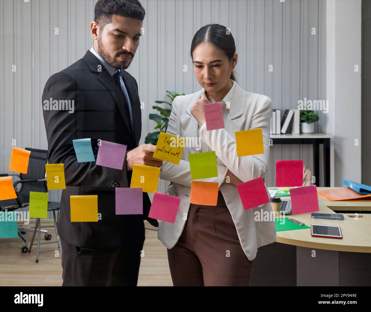 Homme d'affaires en costume noir et collègue rencontre avec des notes de papier collantes sur le mur de verre pour de nouvelles idées. Utiliser une méthodologie agile pour les affaires dans un bureau de start-up technologique. Banque D'Images