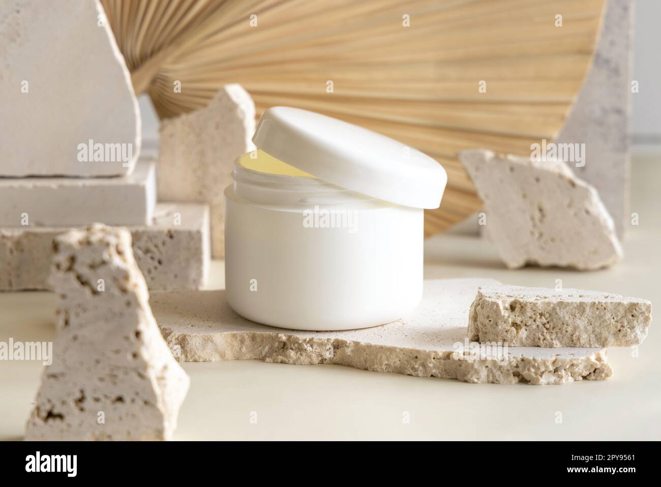 Pot de crème blanche ouvert avec un couvercle sur les pierres de biège contre la feuille de palmier séchée. Maquette cosmétique Banque D'Images