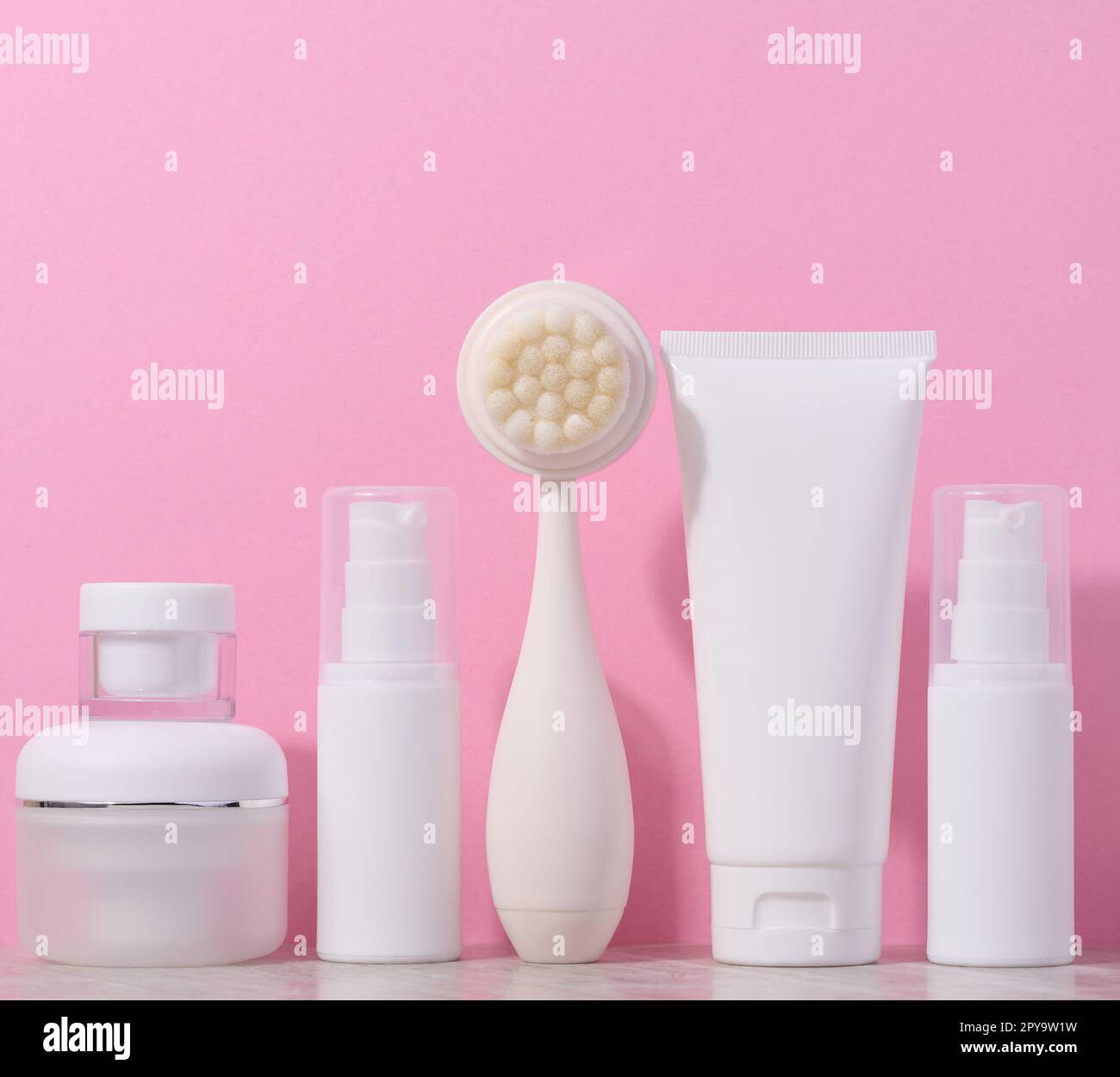 Tubes en plastique blanc et pots de crème, et une brosse de massage pour le nettoyage du visage sur fond rose, des articles pour les procédures cosmétiques Banque D'Images
