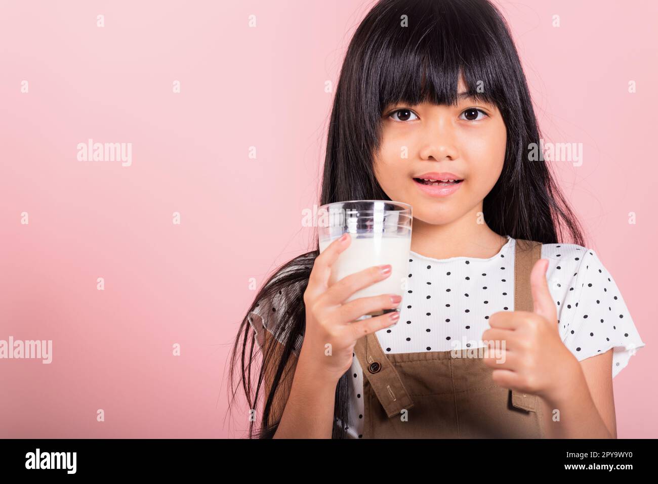 Petit enfant asiatique 10 ans sourire tenir le verre de lait boire du lait blanc et montrer le pouce vers le haut du doigt Banque D'Images