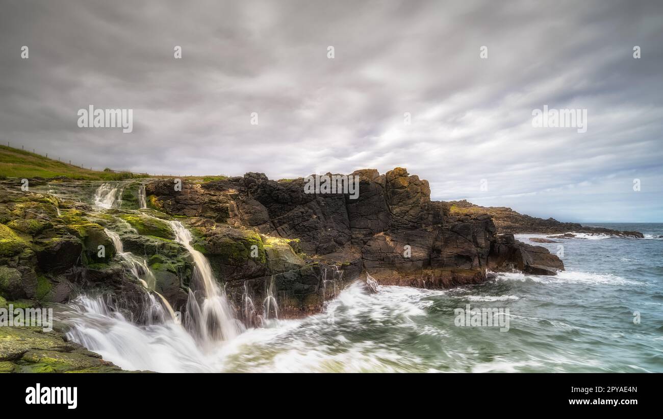 Dunseverick Falls avec de petites falaises et des traînées d'eau tombant dans l'océan Atlantique, Irlande du Nord Banque D'Images