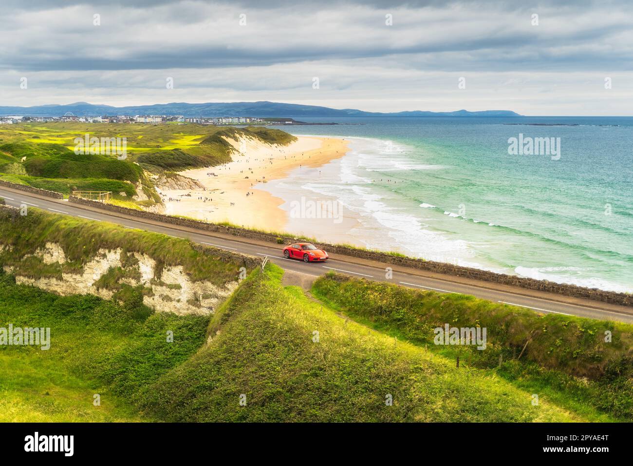 Voiture de sport rouge sur une route avec White Rocks Beach en arrière-plan, Irlande du Nord Banque D'Images