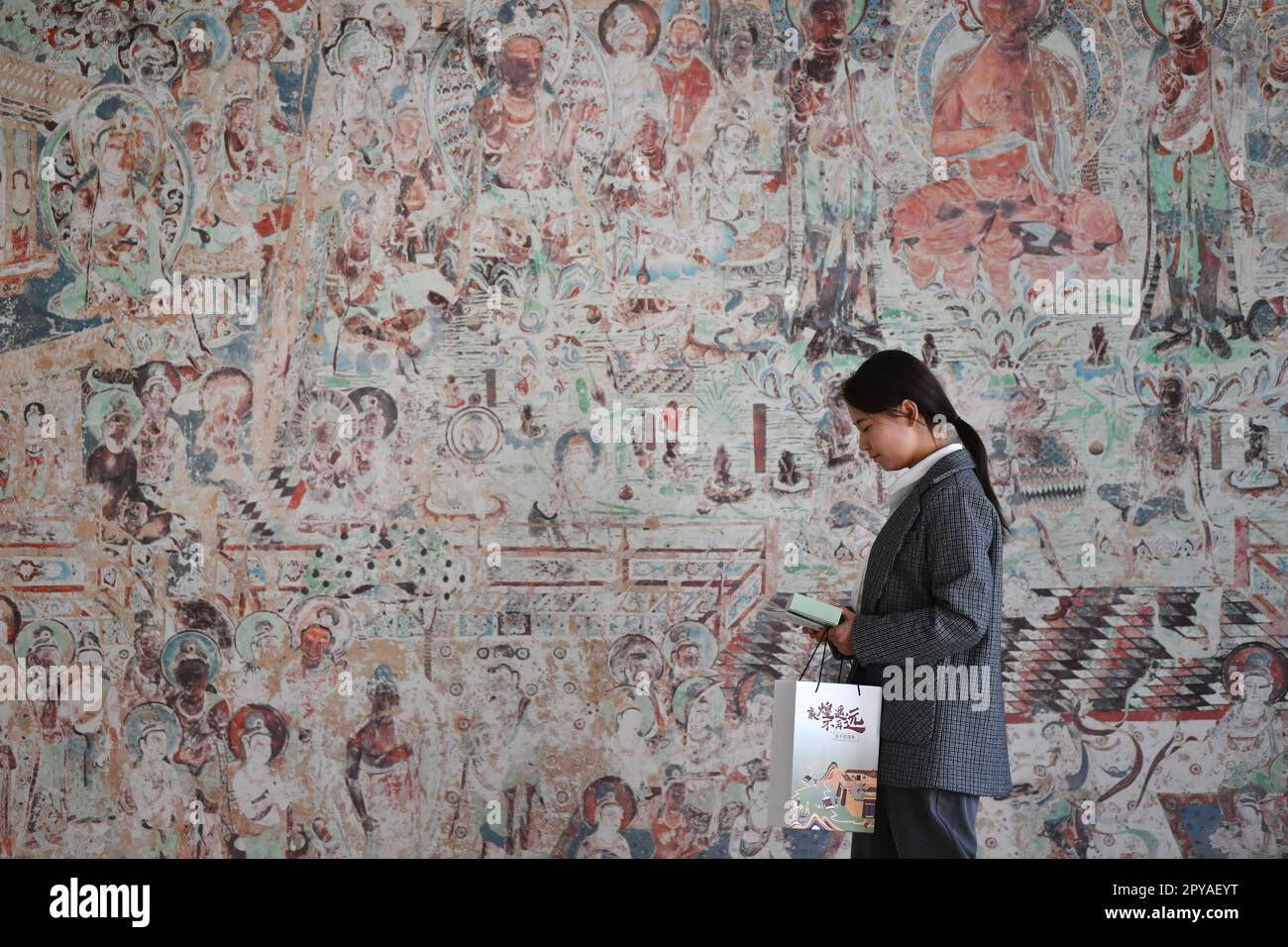 Dunhuang, province chinoise de Gansu. 25th avril 2023. Liao Xueting, un acheteur de l'équipe de préservation numérique de l'Académie Dunhuang, passe devant une réplique haute fidélité d'une murale à Dunhuang, dans la province de Gansu, au nord-ouest de la Chine, à 25 avril 2023. Un groupe de jeunes techniciens a cherché à utiliser la technologie numérique pour assurer la préservation permanente et l'utilisation durable des reliques culturelles dans les Grottes de Mogao, site classé au patrimoine mondial de l'UNESCO à Dunhuang. Crédit : Chen Bin/Xinhua/Alay Live News Banque D'Images