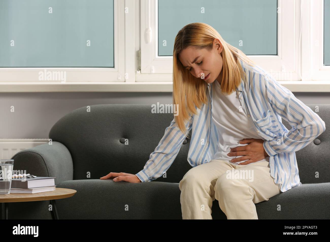 Jeune femme souffrant de douleurs menstruelles sur le canapé à l'intérieur Banque D'Images