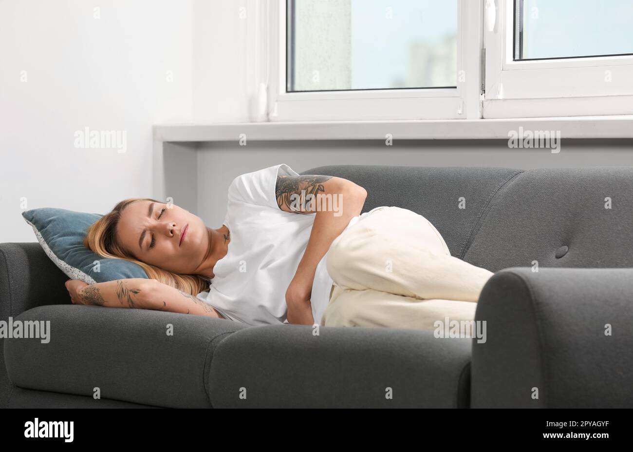 Jeune femme souffrant de douleurs menstruelles sur le canapé à l'intérieur Banque D'Images