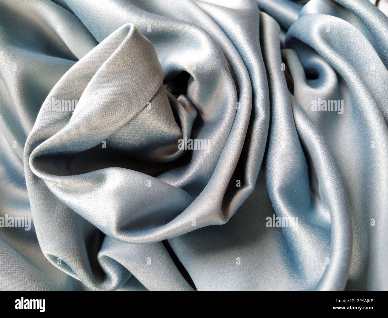 Tissu soyeux au toucher de couleur gris - bleu avec un brillant éclat. Éclairage naturel, lumière et ombre. Le matériau est plié de manière décontractée. Textile polyester. Banque D'Images