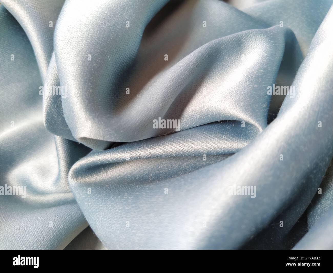 Tissu soyeux au toucher de couleur gris - bleu avec un brillant éclat. Éclairage naturel, lumière et ombre. Le matériau est plié de manière décontractée. Textile polyester Banque D'Images