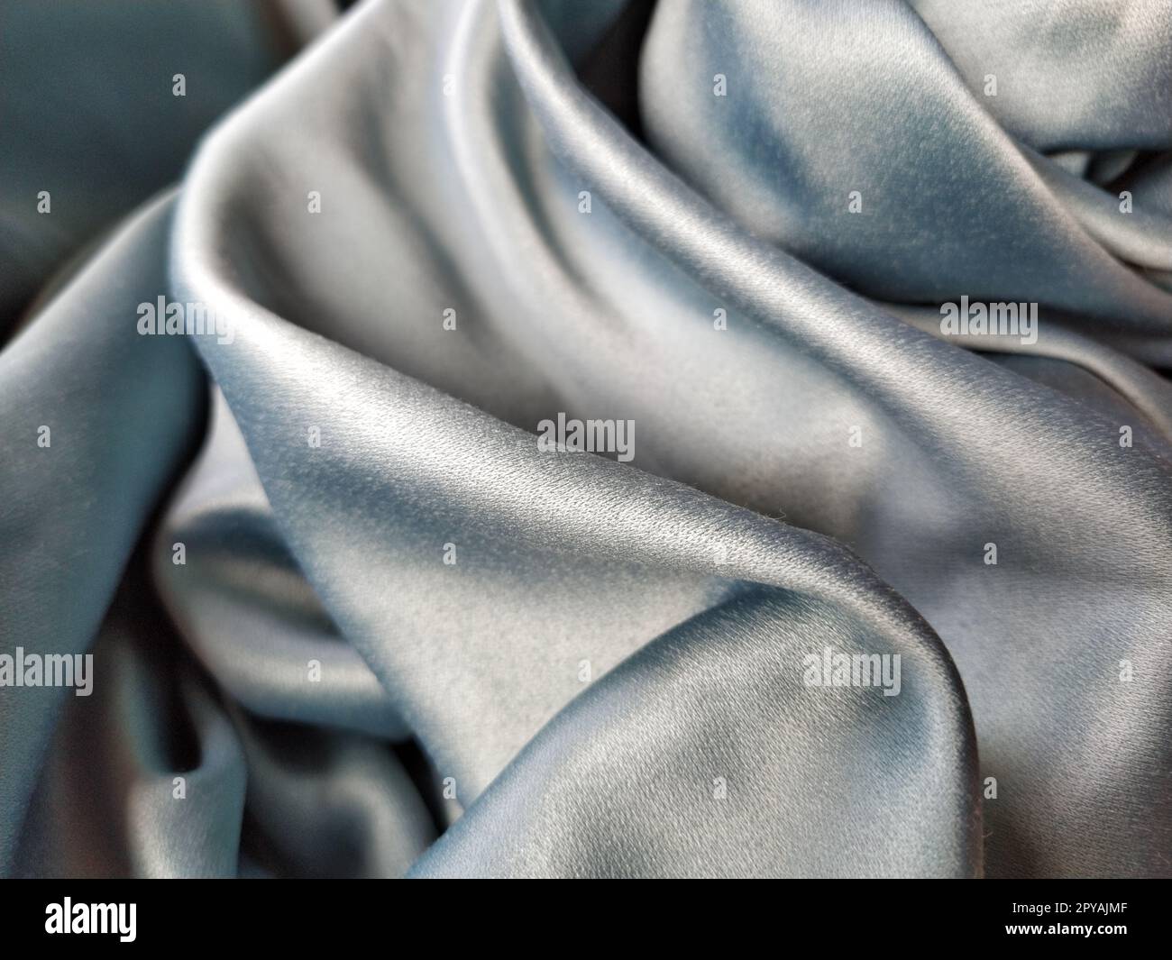 Tissu soyeux au toucher de couleur gris - bleu avec un brillant éclat. Éclairage naturel, lumière et ombre. Le matériau est plié de manière décontractée. Textile polyester Banque D'Images