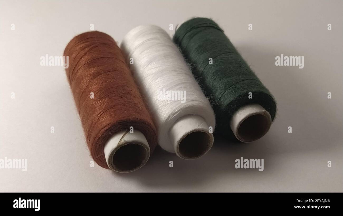 Bobines et bobines de fil de différentes couleurs - marron, blanc et vert. Gros plan. Lumière naturelle sur le côté gauche. Skeins de fil. Fournitures de couture. Banque D'Images