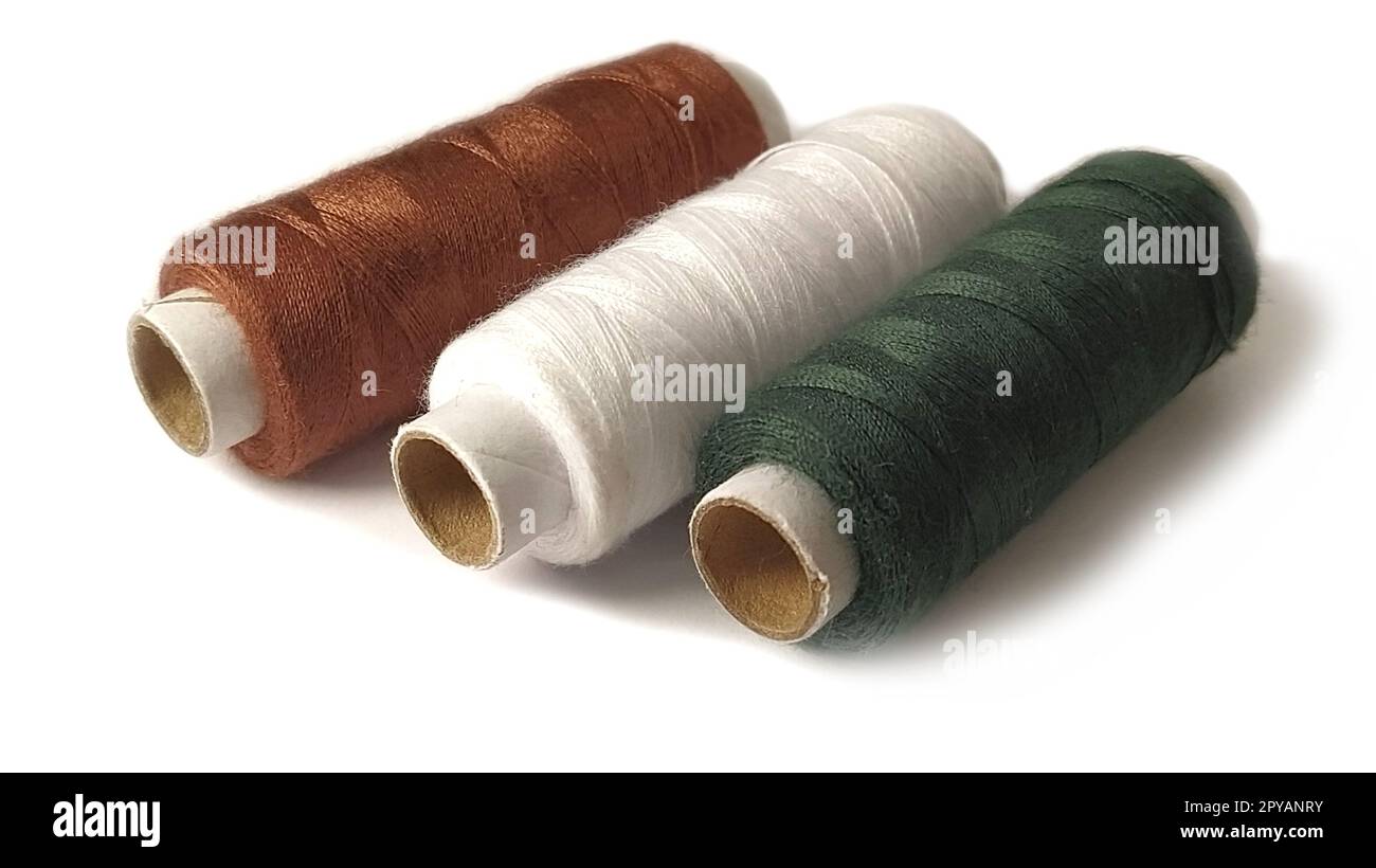 Bobines et bobines de fil de différentes couleurs : marron, blanc et vert. Gros plan. Lumière naturelle sur le côté gauche. Isoler sur un fond blanc avec une ombre claire. Skeins de fil. Fournitures de couture Banque D'Images