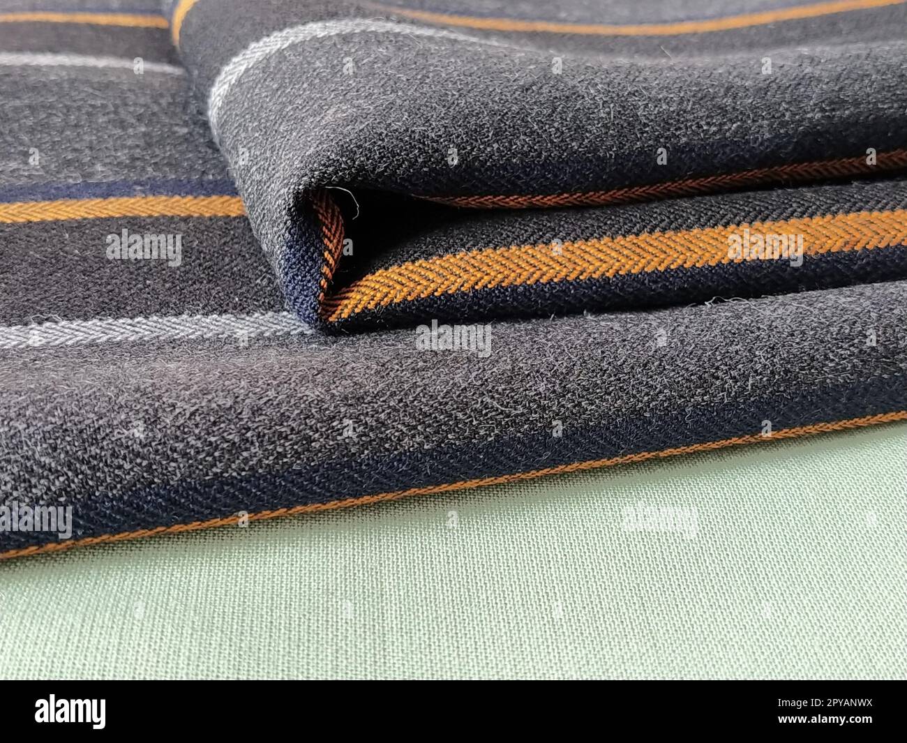 Tissu plié vert clair et noir-gris avec rayures orange et bleu foncé. Décoration intérieure. Habiller les tissus dans un style décontracté. Matériau dense pour rideaux d'intérieur et finition de meubles Banque D'Images
