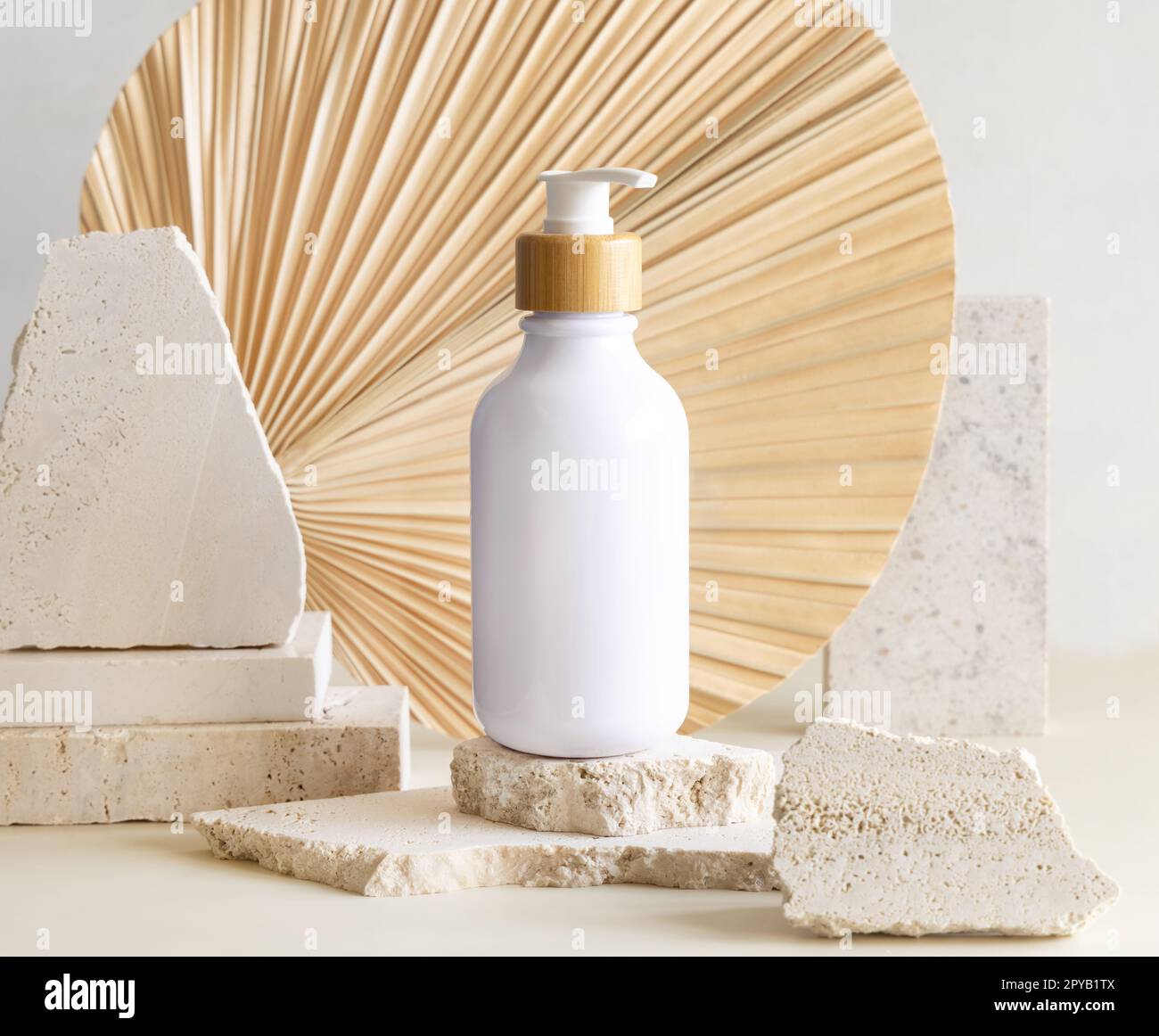 Blanc une bouteille de pompe sur des pierres de biège contre la feuille de palmier séchée. Maquette cosmétique Banque D'Images