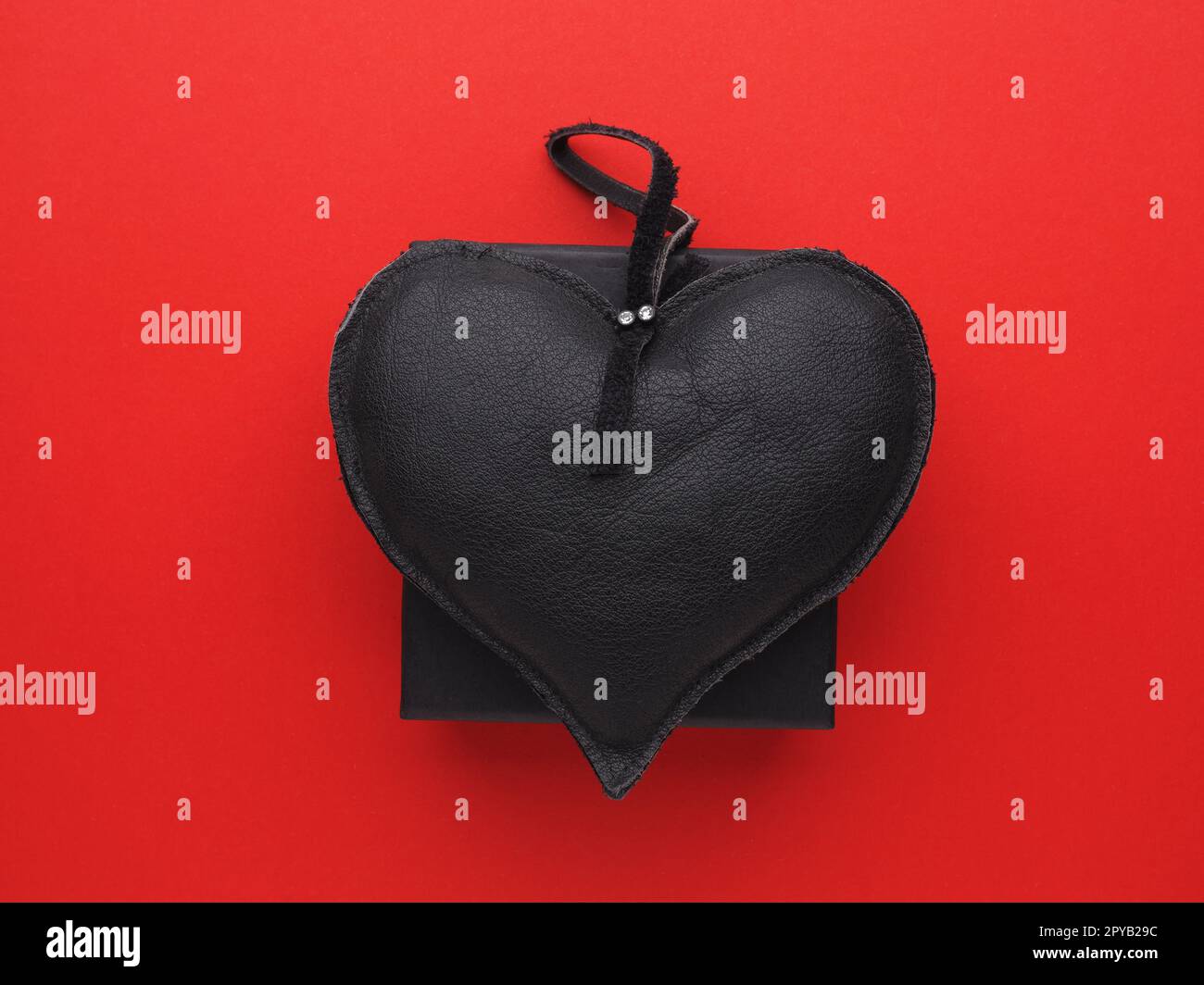 Coeur en cuir noir sur une boîte cadeau noire sur fond rouge, Saint Valentin ou anniversaire Banque D'Images