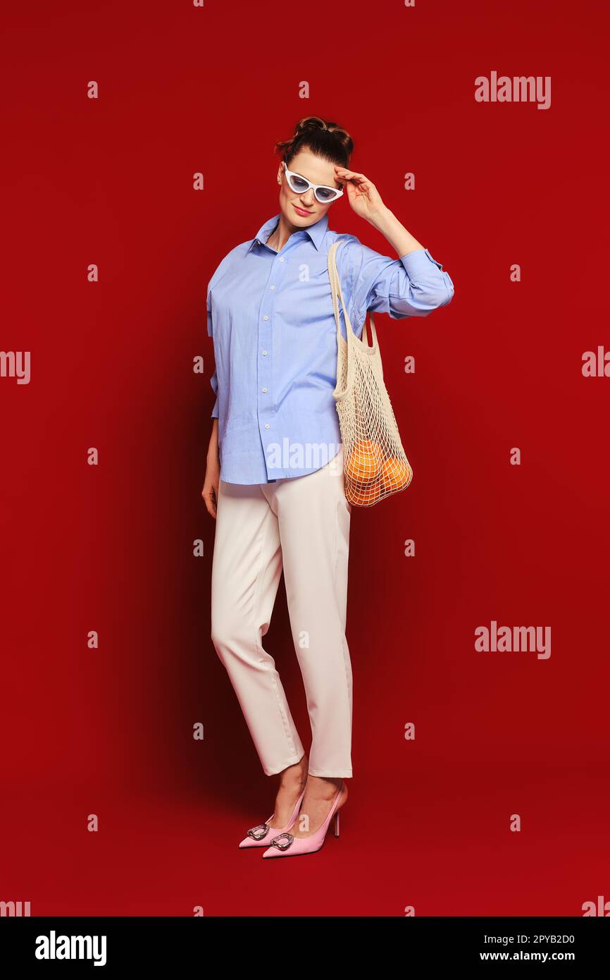 Femme avec des oranges dans un sac de corde réutilisable sur l'épaule touchant ses lunettes de soleil Banque D'Images