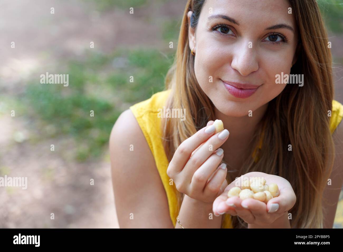 Une fille en bonne santé piquant des noix de macadamia de sa main dans le parc. Regarde la caméra. Banque D'Images