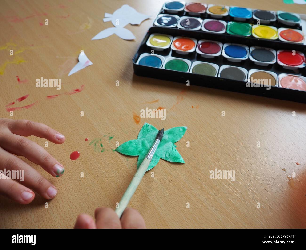 Bureau avec outils de dessin. Ensemble de peintures à l'aquarelle. Figurines de poisson peintes découpées en papier. Vue d'en haut. Leçon ou tâche créative. La main de l'enfant avec un pinceau peint une étoile Banque D'Images