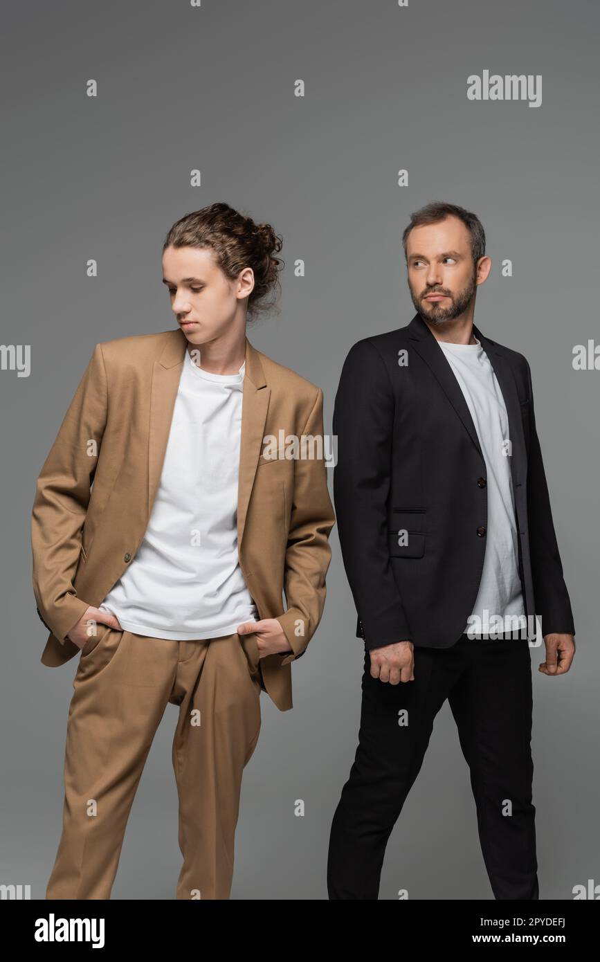 garcon adolescent bien habille en costume beige debout avec les mains dans les poches a cote du pere barbu isole sur image grise Photo Stock Alamy