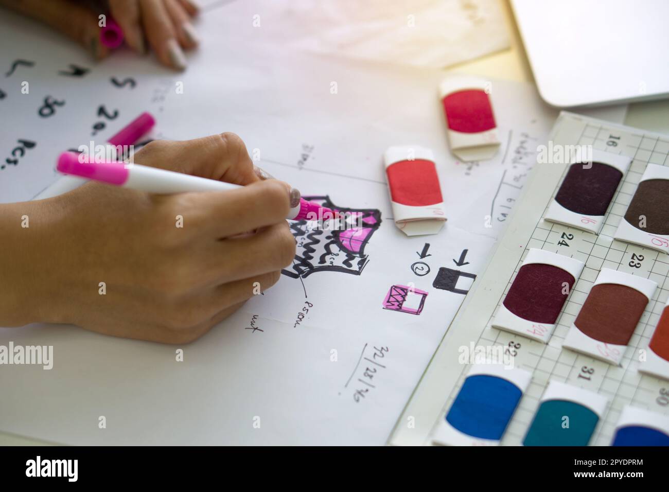 Gros plan mode designer main utiliser Magic stylo peinture sur le motif pour le tissu. Des échantillons de tissus aux couleurs vives sont disponibles sur l'établi. Banque D'Images