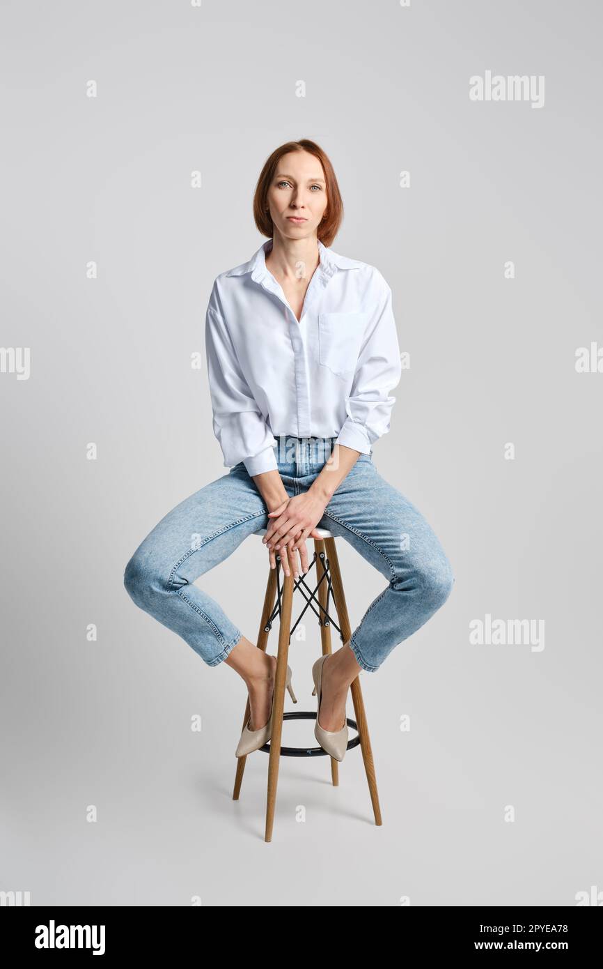 Portrait d'une femme rousse caucasienne d'âge moyen en chemise blanche et jeans bleus Banque D'Images