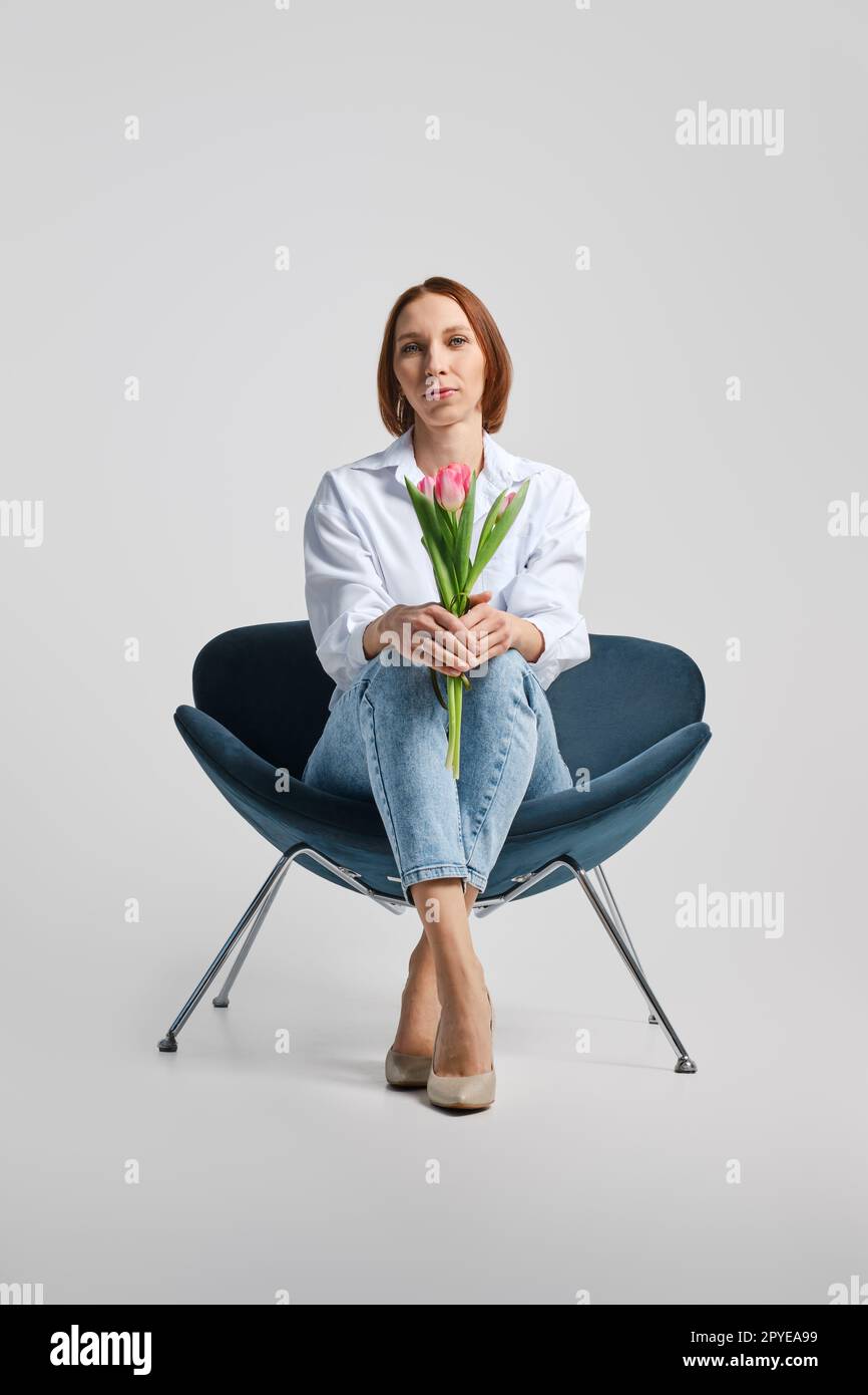 Vue à angle bas à la femme positive d'âge moyen assise dans un fauteuil avec des tulipes Banque D'Images