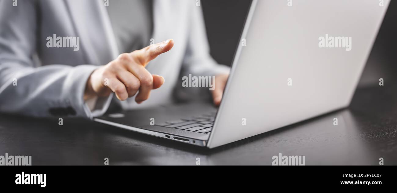 Femme d'affaires assise à la table noire et pointant du doigt sur l'écran de son ordinateur portable. Banque D'Images