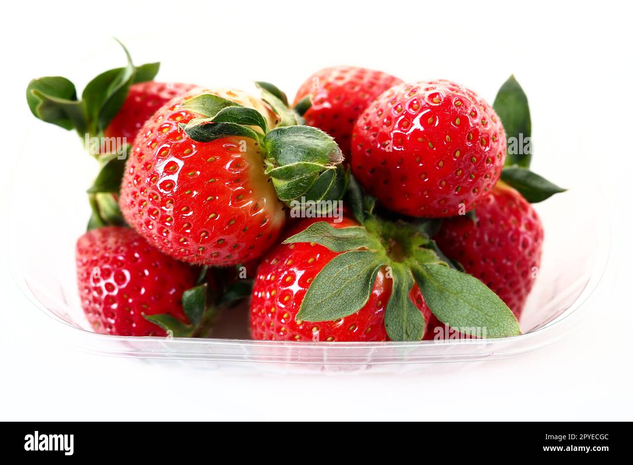 Fraises mûres dans un emballage en plastique sur fond blanc. Délicieuses baies fraîches dans un récipient à vendre aux clients. Garder les aliments frais. Aliments sains, vitamines et micro-éléments. Banque D'Images