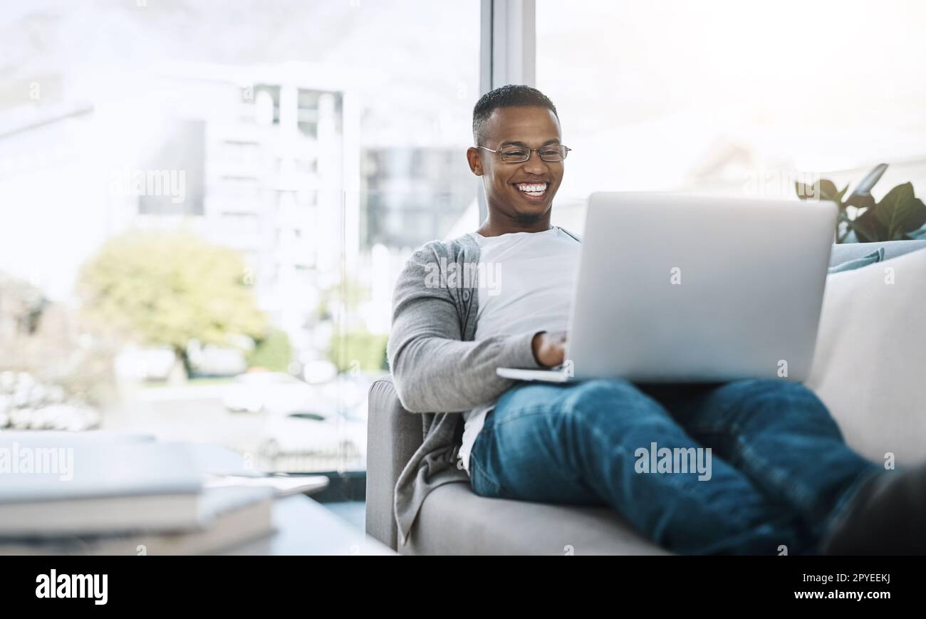 Parfois, il vous suffit de vous détendre. un beau jeune homme utilisant son ordinateur portable tout en étant assis sur un canapé à la maison. Banque D'Images