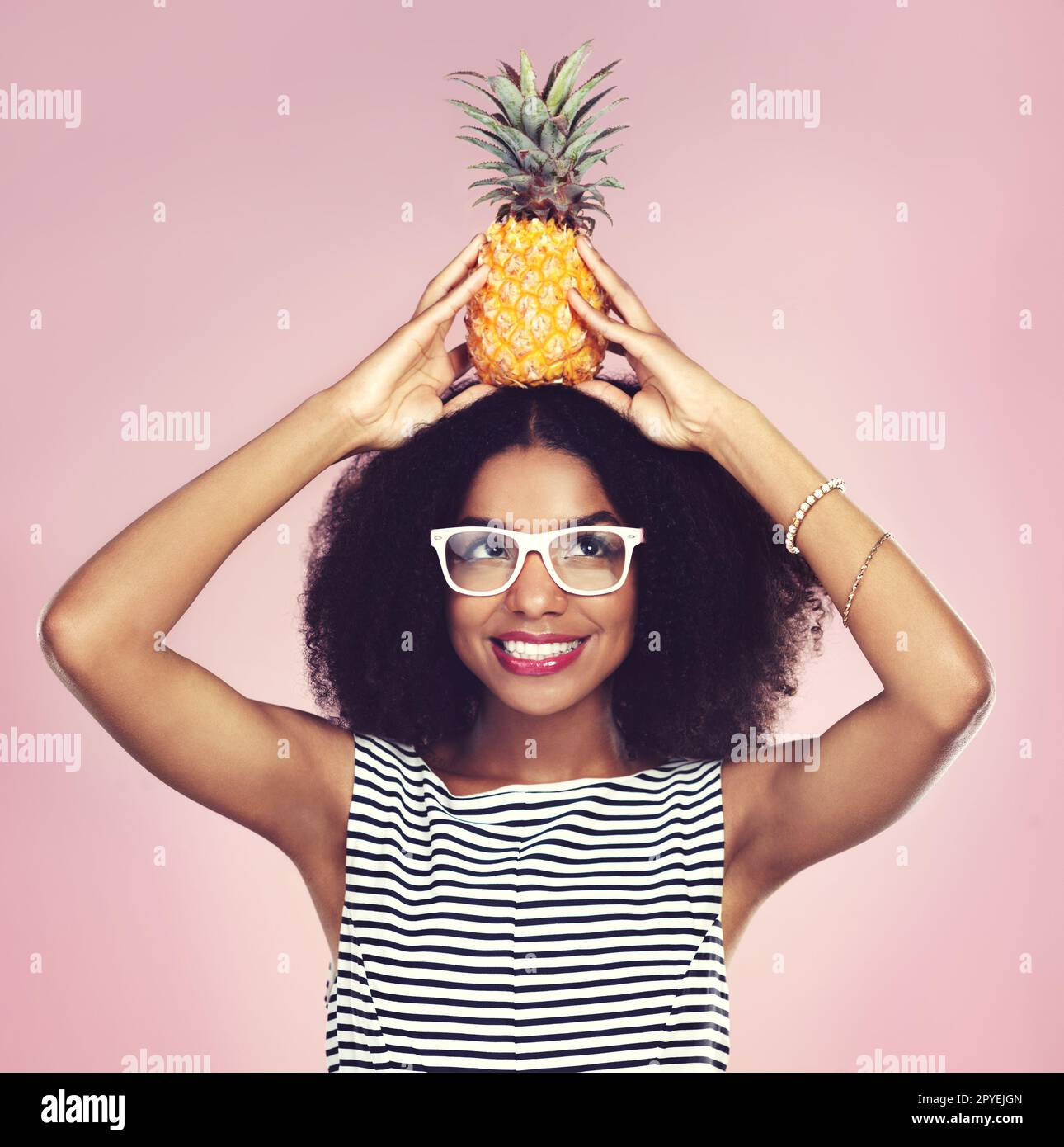 Piquant à l'extérieur mais doux à l'intérieur. Photo studio d'une belle jeune femme posant avec un ananas sur sa tête. Banque D'Images