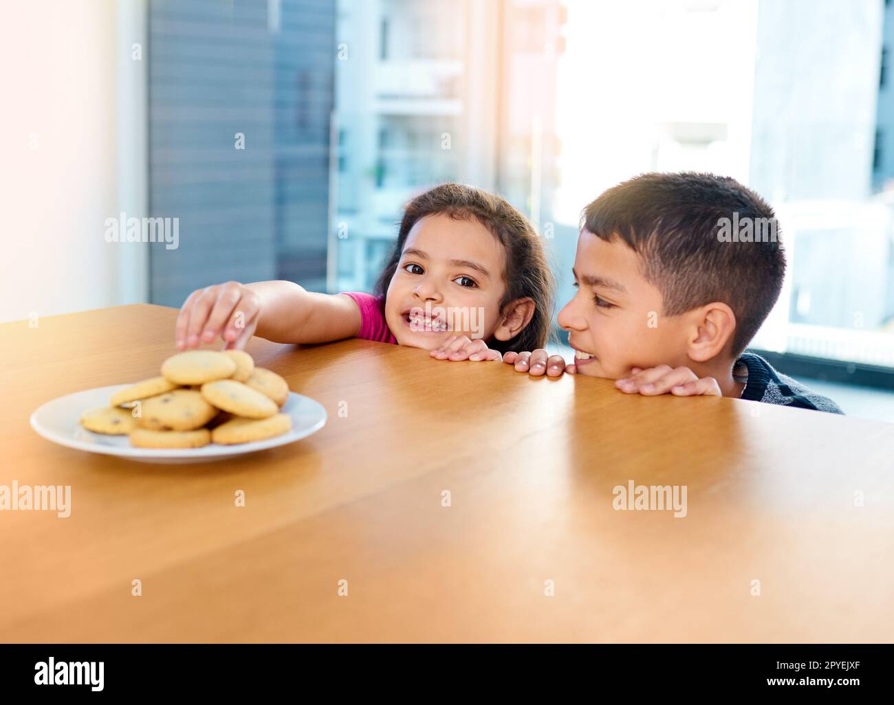 Ses petits doigts sont méchants. deux jeunes enfants espiègles volent des biscuits sur la table de cuisine à la maison. Banque D'Images