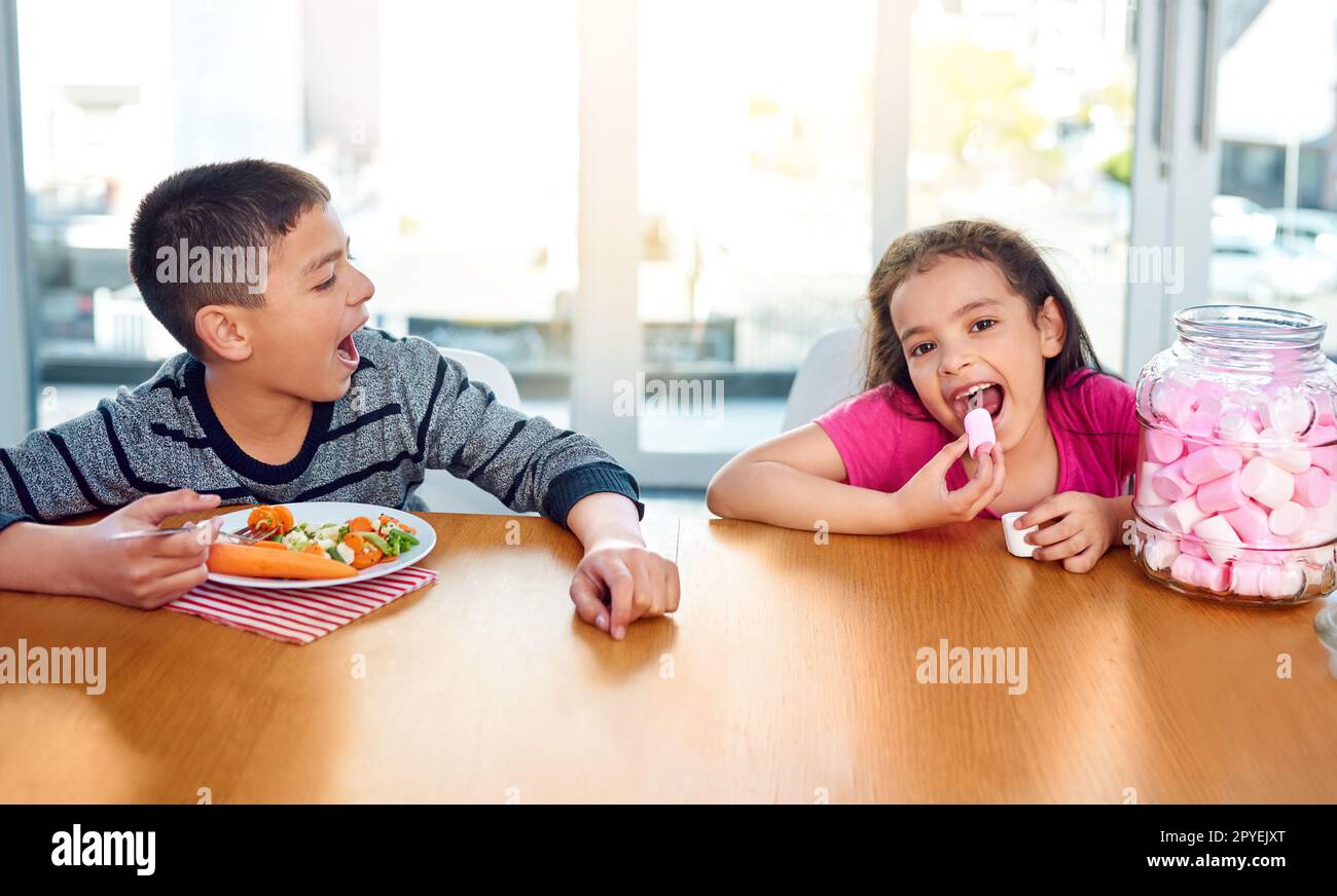 C'est totalement injuste. un jeune garçon malheureux criant parce qu'il doit manger des légumes pendant que sa sœur a des guimauves à la maison. Banque D'Images