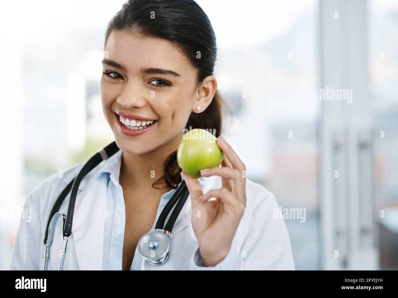 La bonne santé est tout au sujet de ce que vous mangez. Portrait d'une jeune femme médecin tenant une pomme. Banque D'Images