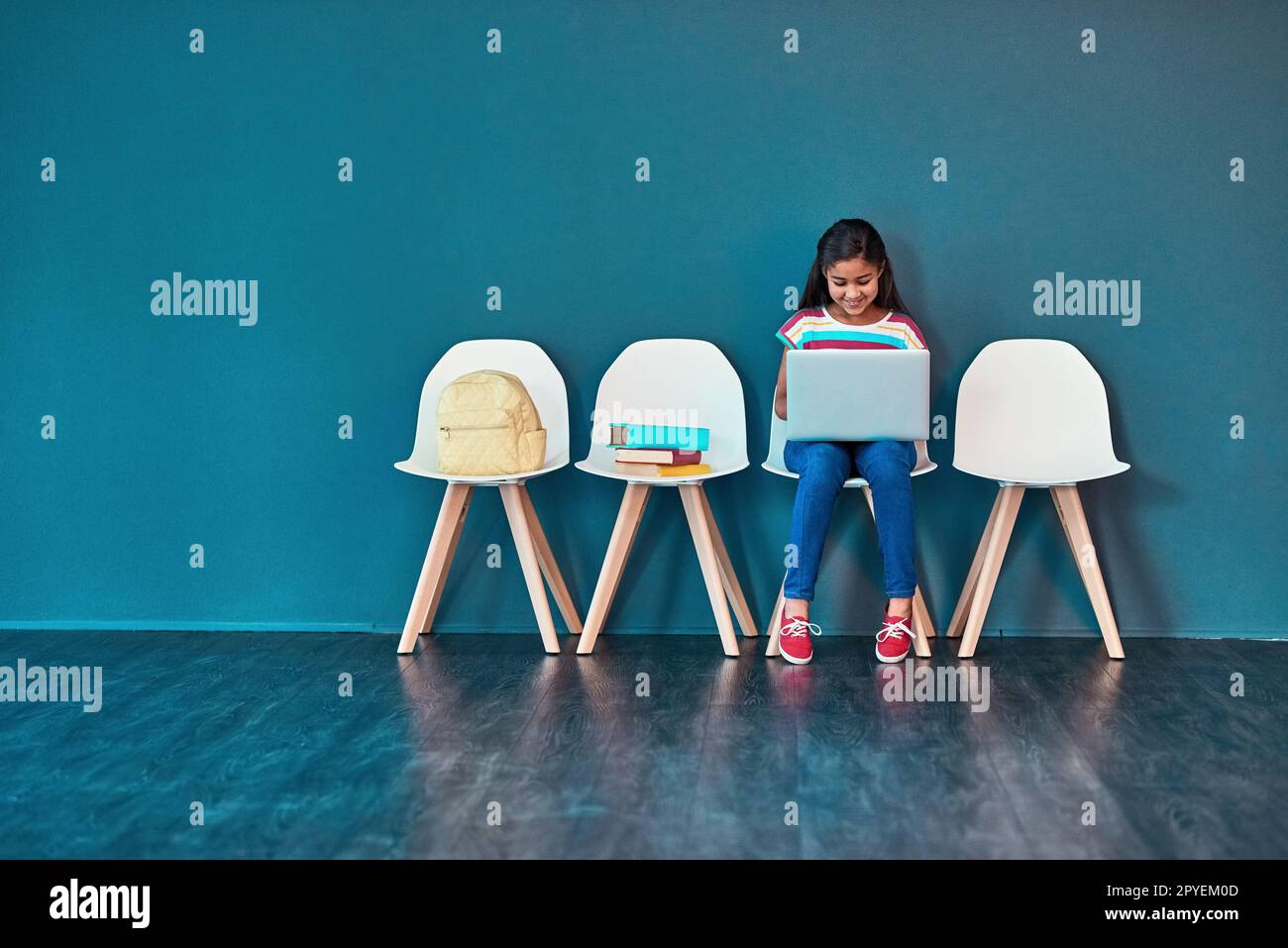 Apprentissage en ligne. Photo studio d'une jeune fille assise sur une chaise et utilisant un ordinateur portable sur fond bleu. Banque D'Images