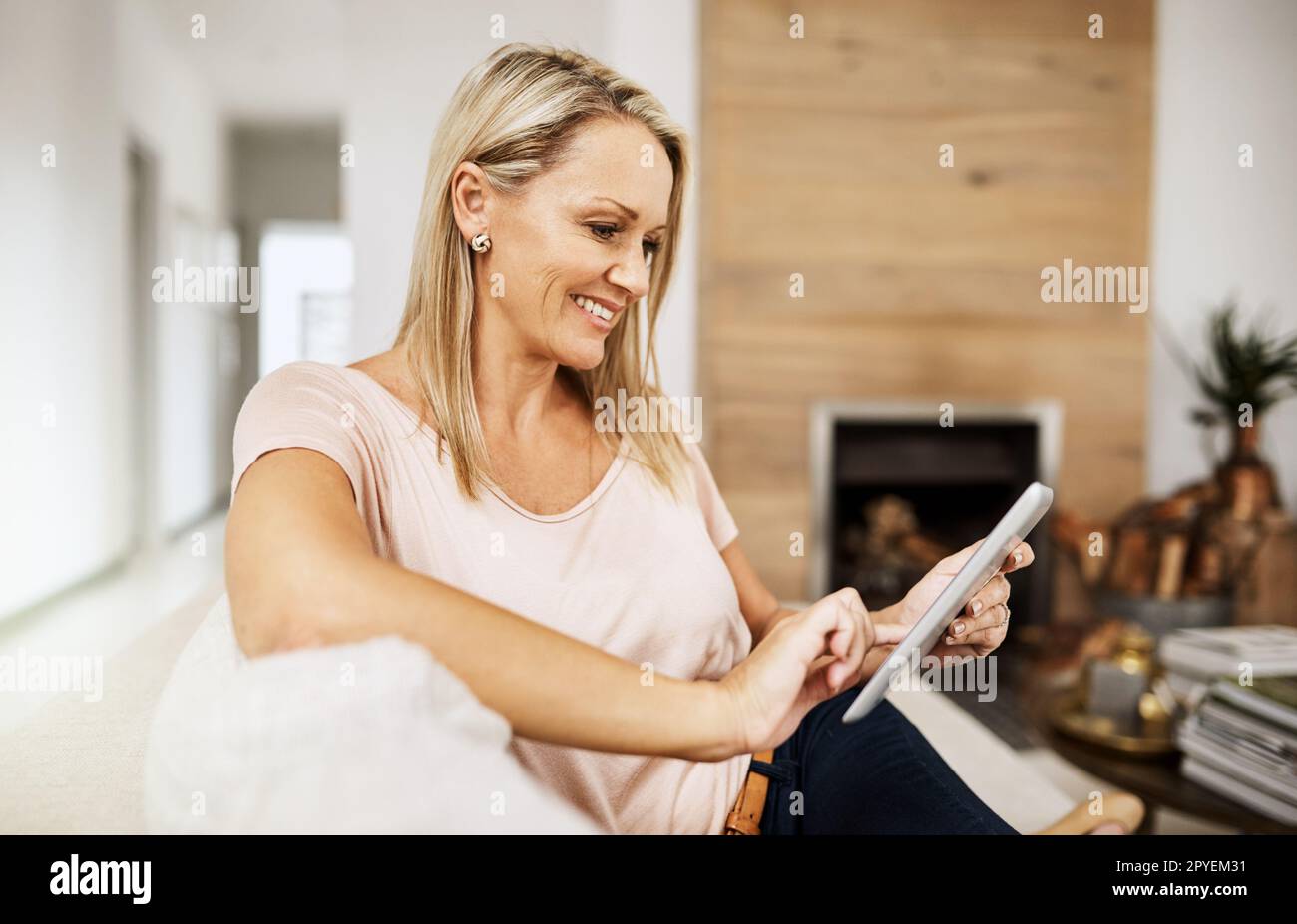 Voyons si je peux trouver mes anciens amis en ligne. une femme mûre utilisant sa tablette numérique tout en se relaxant sur son canapé à la maison. Banque D'Images