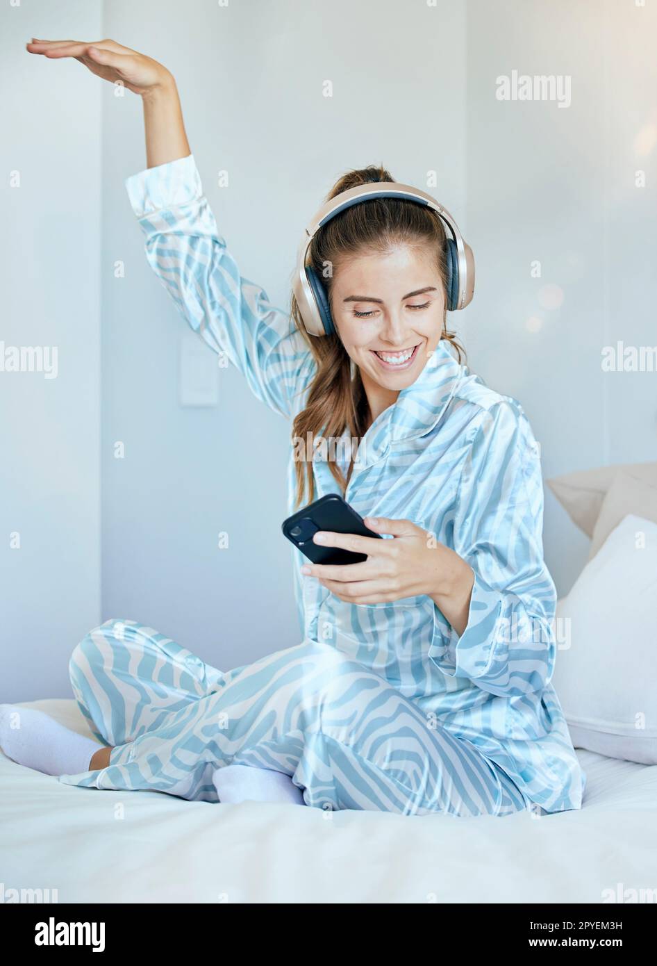 Écouteurs, téléphone et femme au lit dansant tout en écoutant de la musique, une playlist ou la radio chez elle. Heureux, sourire et jeune femme du Canada en pyjama en streaming audio, album ou chanson avec un téléphone portable. Banque D'Images