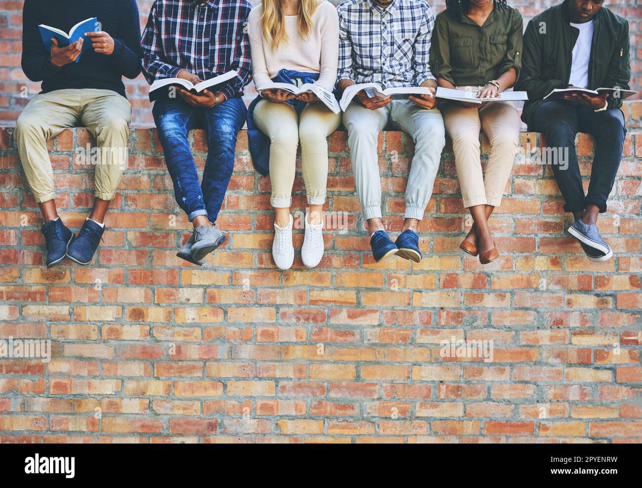 Étudier maintenant, profit plus tard. un groupe d'étudiants universitaires méconnaissables étudiant en s'asseyant à l'extérieur sur un mur de briques faciès. Banque D'Images
