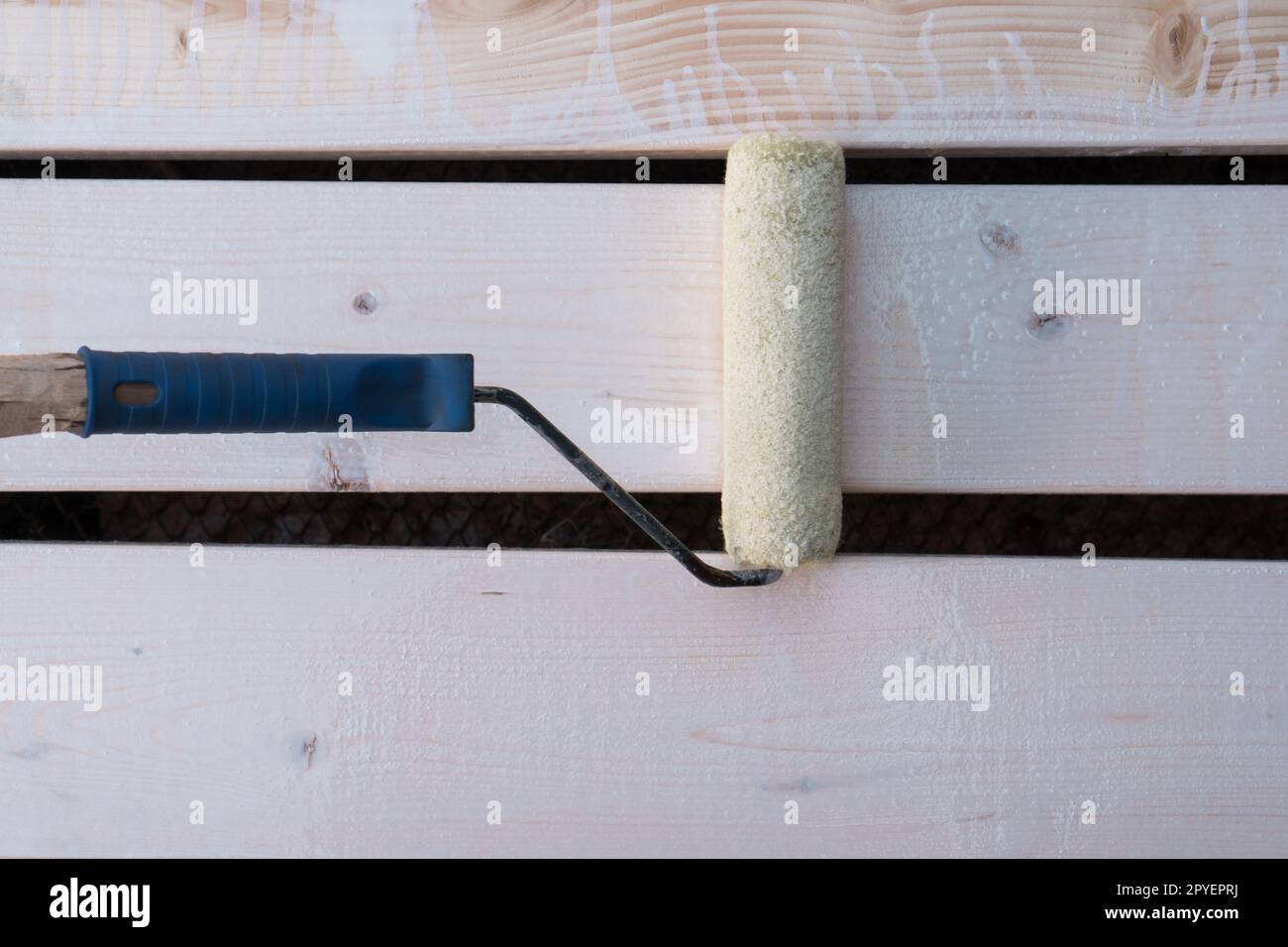 Pinceau applicateur de rouleau de peinture blanc avec poignée peignant clôture en bois, planche de plancher. Réparation cosmétique, rénovation de maison Banque D'Images