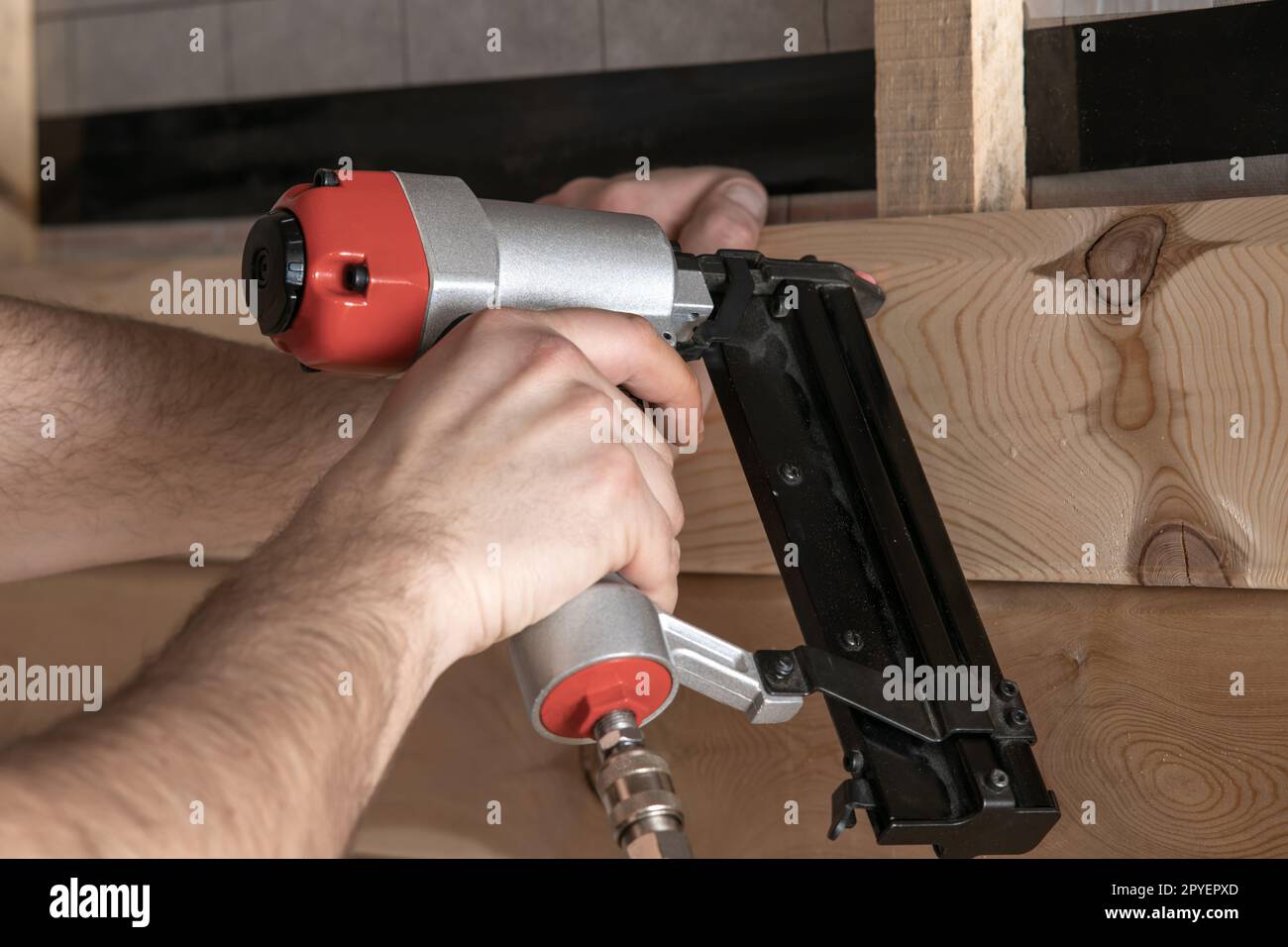 Gros plan les mains masculines recadrées utilisent une cloueuse pneumatique, un pistolet à clous agrafeuse pour planche et planche en bois. Vue première personne du constructeur Banque D'Images