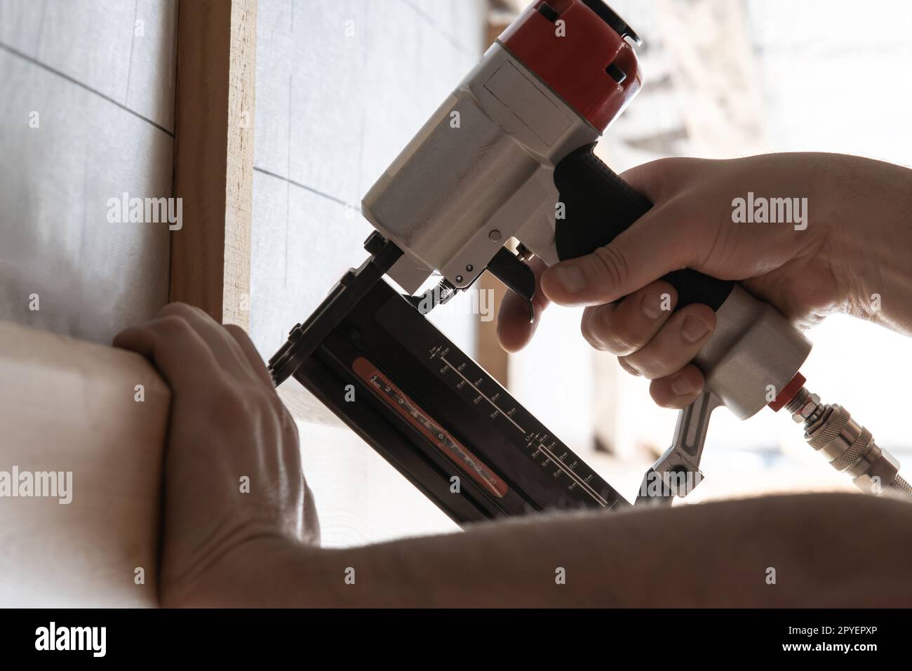 Gros plan les mains masculines méconnaissables utilisent une cloueuse pneumatique, un pistolet agrafeur pour planche en bois en plein air. Construire maison, travail de charpentier Banque D'Images