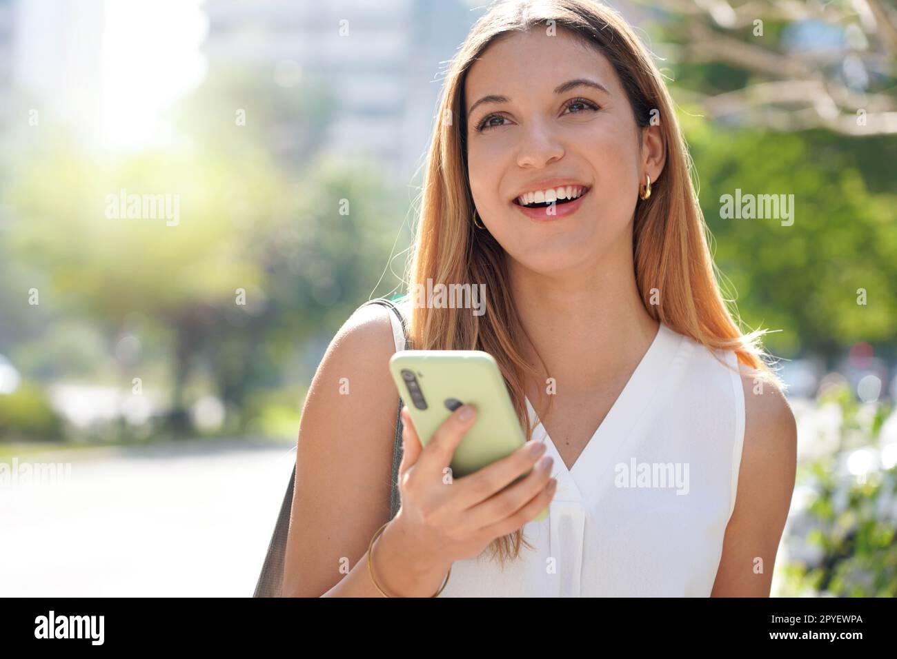 Gros plan de rire femme décontractée regardant loin tenant son téléphone mobile à l'extérieur Banque D'Images
