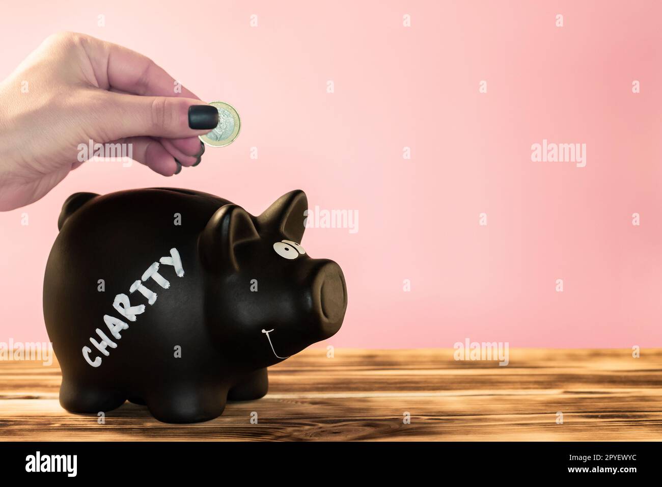 Main mettre une pièce dans une tirelire noire avec une étiquette de charité craie sur un fond rose, don et concept de charité. Banque D'Images