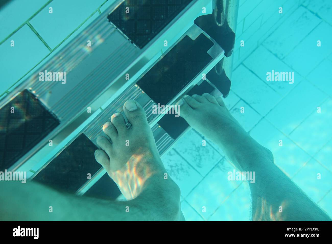 Photo sous-marine, l'homme marchant sur les pieds des escaliers de la piscine. Banque D'Images