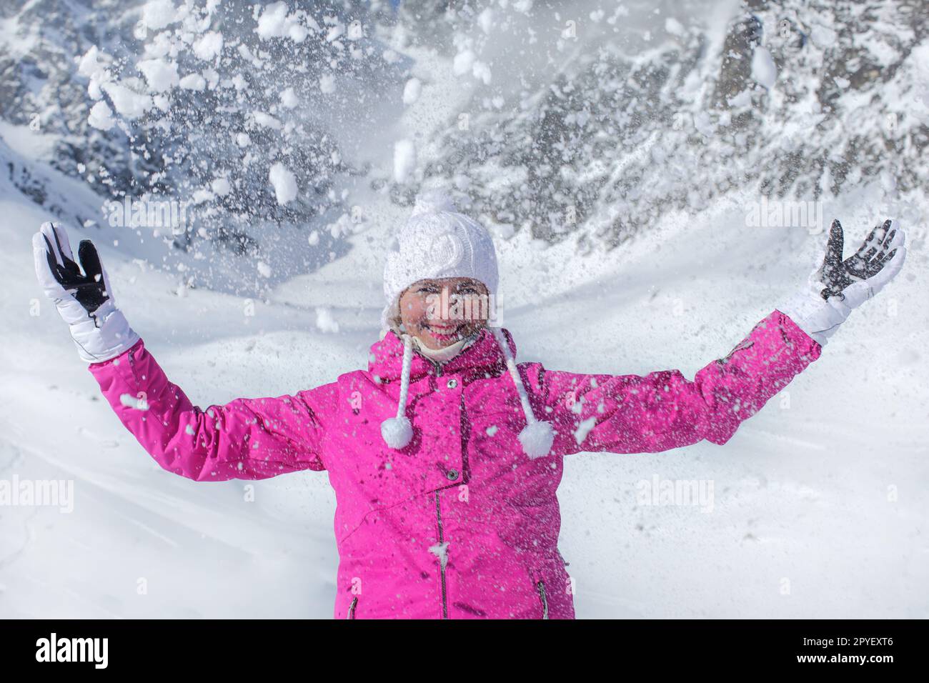 Jeune femme en rose veste de ski, gants et chapeau d'hiver, smiling, jeter de la neige dans l'air Banque D'Images