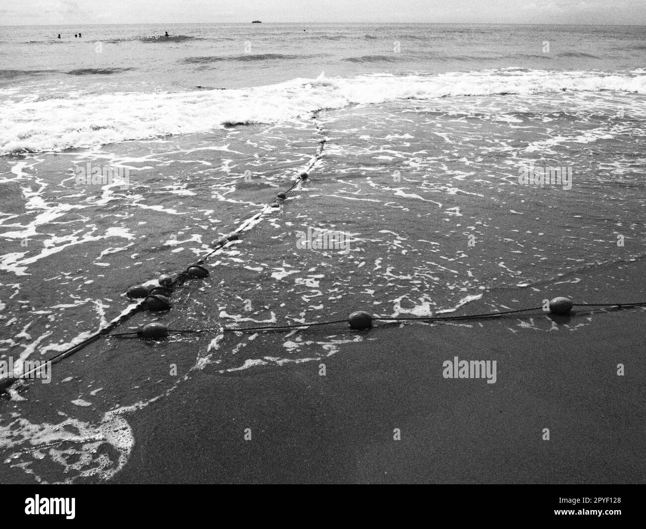 Bouées sur une corde près de l'eau de mer. Les bouées de sauvetage se contentent d'alerter les gens de la profondeur de l'eau. Délimitant un lieu sur une plage de sable entre les hôtels. Vague avec des bulles. Photo noir et blanc monochrome Banque D'Images